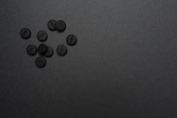 Primer plano de áspero negro redondo píldoras absorbente de carbono yacen en una superficie gris oscuro — Foto de Stock