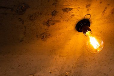 Tavandaki kahverengi arka planda bir elektrik lambası parlıyor..