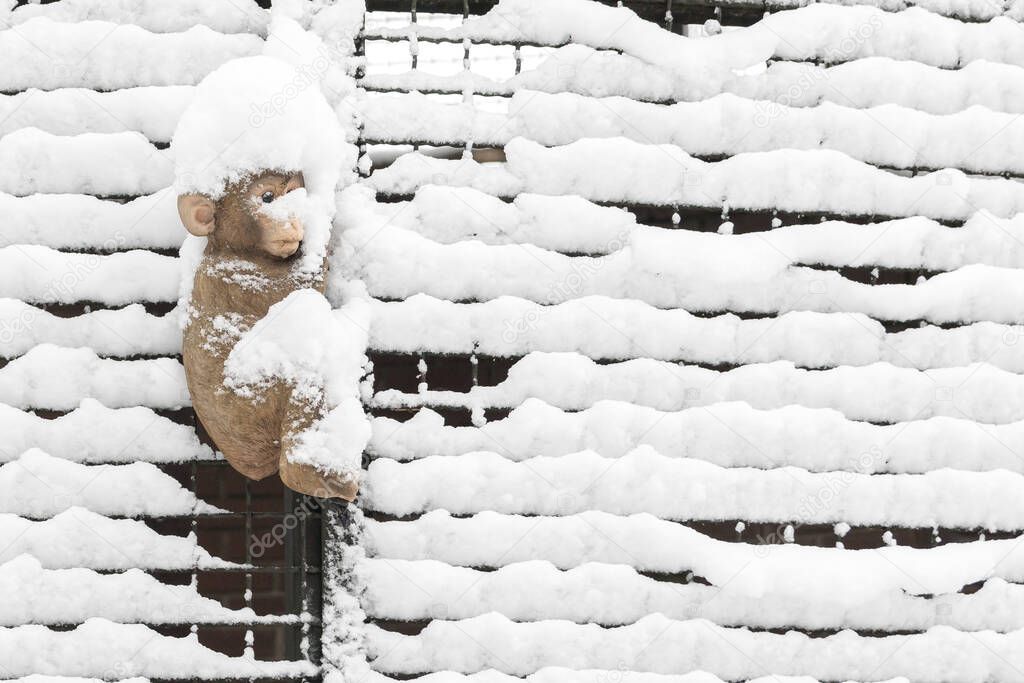 Toy monkey in the snow on a background of a metal grill.