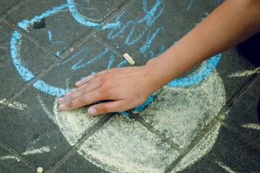 Bir çocuğun eli güneşi ve asfaltı tebeşirle boyar..