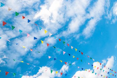 Bulutlu mavi gökyüzüne karşı çok renkli bayraklar ve bir kilise kubbesi..