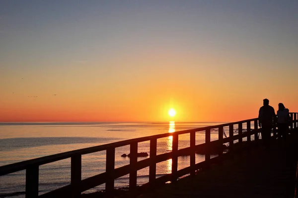 Duas Pessoas Observam Pôr Sol Uma Passarela Madeira Longo Mar — Fotografia de Stock