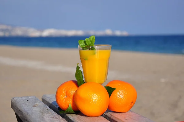 三个橙子 叶子和一杯橙汁在一张木桌上 背景模糊 蓝天的城市 — 图库照片