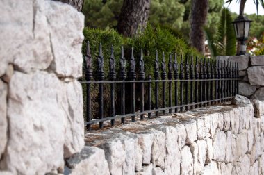 Metal elementli taş çit ve yeşil ağaçlı dekoratif fener.