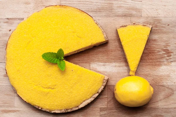 Lemon pie in the form of Pacman, a triangular piece of cake and lemon on a wooden board.