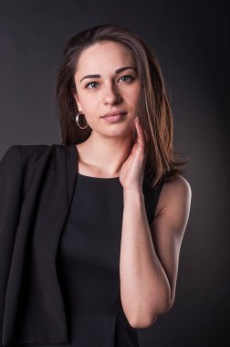 Ciddi genç bayan karanlıkta poz veriyor ve boynuna dokunuyor. Zarif siyah elbise, her yer karanlık. Çekici görünümlü harika bir kız.