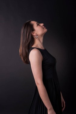 Karanlıkta yukarı bakan hoş bir bayanın profili. Zarif siyah elbise, her yer karanlık. Çekici görünümlü harika bir kız.