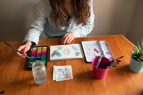 Lady mixing colors during a leaves painting session using watercolor technique from high-angle shot