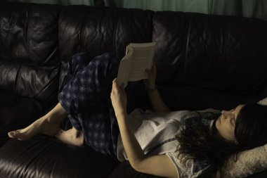 Genç bayan oturma odasında kitap okurken deri kanepesine uzandı.