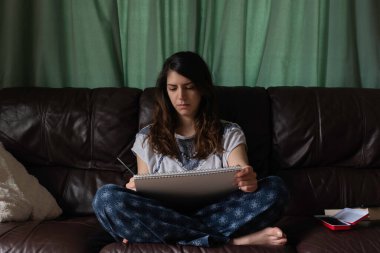 Deri kanepesinde çizim yapan çapraz bacaklı bir kadın.