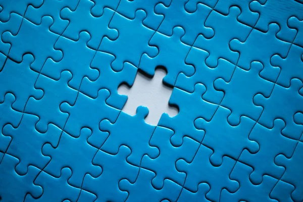 Incomplete blue piece puzzle with a missing piece over a white surface