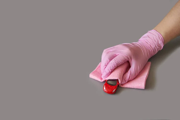 Kırmızı oyuncak arabayı tutan pembe eldiven. Güvenlik antivirüsü ve toz konsepti. Anne çocuk odasında antibakteriyel temizlik yapıyor. Anti virüs hijyen prosedürü. Gri arkaplan