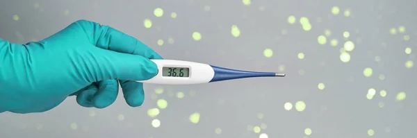hand in green glove holds thermometer normal temperature