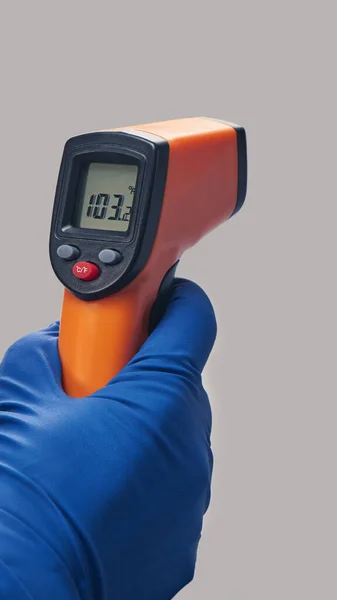 hand in blue glove holds ir thermometer high temperature