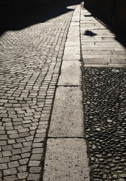 Detail of the pavement of a street in the center of Vicenza. Square elements in basaltic stone, curb and sidewalks in rectangular slabs. Late afternoon light, shadows stretching across the street.