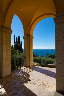 Vittoriale degli Italiani kemerleri Garda Gölü 'ne bakıyor. Binalar açık turuncu ve ahtapottur. Suyun derin maviliğiyle harika bir kontrast oluşturan renkler. Gardone Riviera.