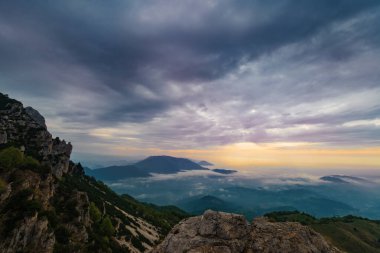 Venedik dağlarından Piccole Dolomiti adı verilen bulutlu bir gün doğumu. Alçak bulutlar ovayı kaplıyor, sadece tepelerin tepeleri görülebiliyor. Ufuktaki ışık çizgisi. Vicenza, İtalya.