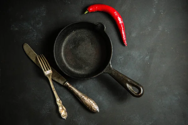 Gri arka planda kızartma tavası, biber, çatal ve bıçak.