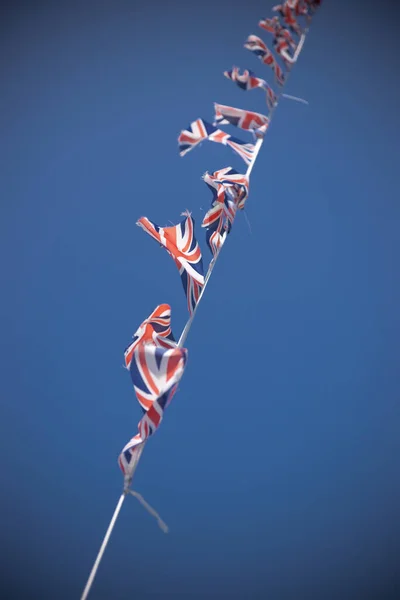 A line of Union Flag (Union Jack) bunting blowing in the wind against a blue sky.