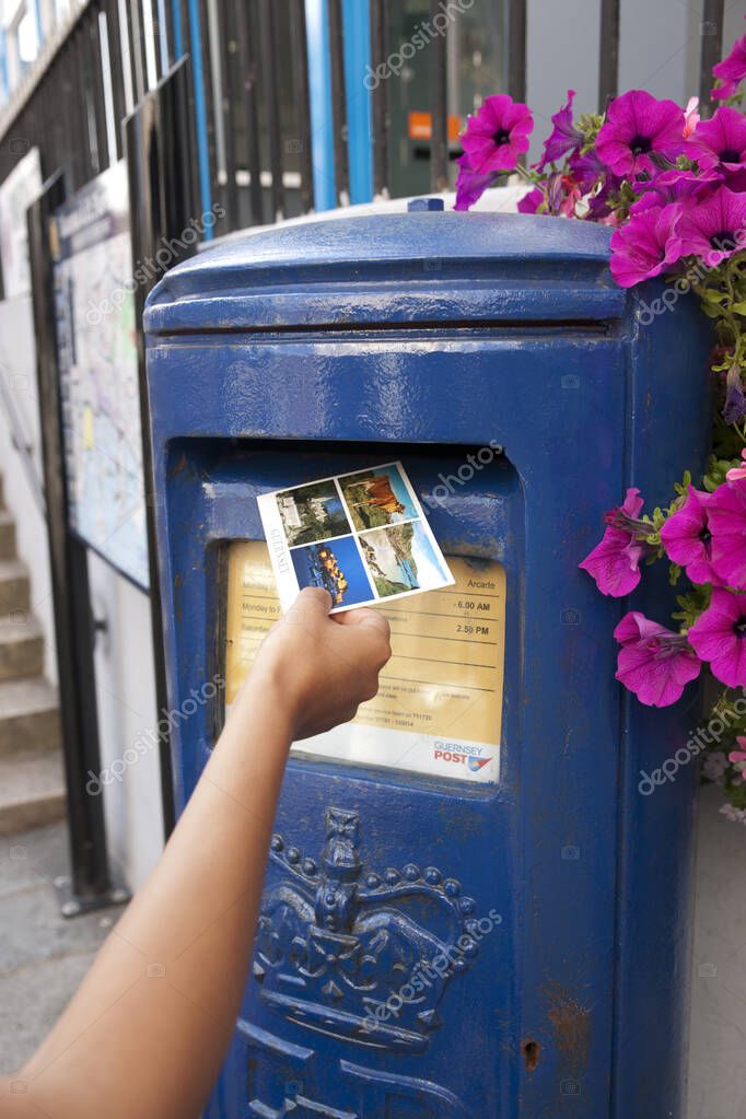 A Hand putting a postcard in a Blue Guernsey Post Box unique to Guernsey in the town of St Pierre Port (St Peter Port), the main settlement of Guernsey, The Channel Islands, UK - 11th July 2013