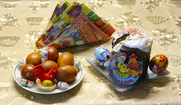 Paskalya tatili. Tabakta paskalya pastası. Tatil etiketli yumurtaların yanında renkli yumurta resmi olan altlıklar. Evdeki mutluluğun yazıtları. Bir fincan tabağında güzel bir renge boyanmış yumurta. Altın yumurtayla yuvada bir tavuk.