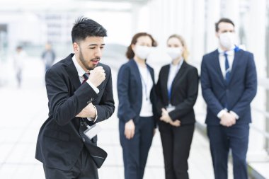 İş adamı elini tutup maske takmadan öksürüyor.