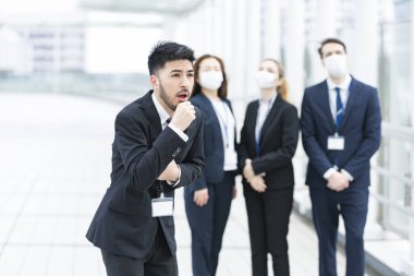 İş adamı elini tutup maske takmadan öksürüyor.