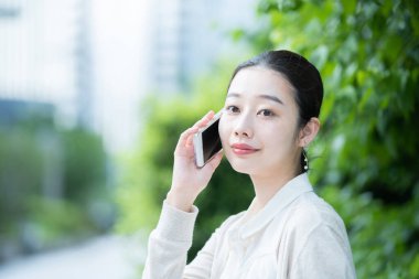 Asyalı genç bir kadın kulağında akıllı telefon olan biriyle konuşuyor.