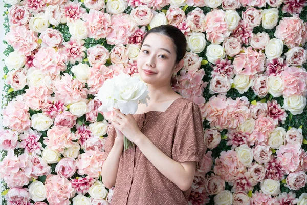 Portrait of young Asian (Japanese) woman standing in front of screen full of flowers