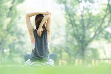 Yeşillerle dolu parkta yoga yapan Asyalı genç kadın.