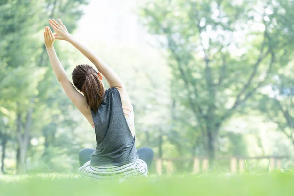 Yeşillerle dolu parkta yoga yapan Asyalı genç kadın.