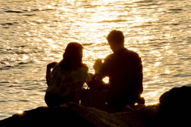 Genç aşıkların silueti ve gün batımında parlayan deniz.