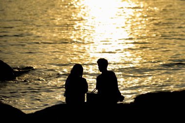 Genç aşıkların silueti ve gün batımında parlayan deniz.