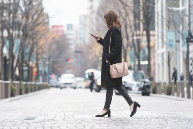 Şehrin sokaklarında akıllı telefon kullanan genç bir kadın.