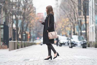 Şehrin sokaklarında akıllı telefon kullanan genç bir kadın.