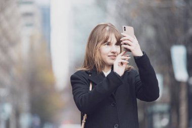 Akıllı telefon kullanan, fotoğraf çeken ve uygulamalar kullanan genç bir kadın.