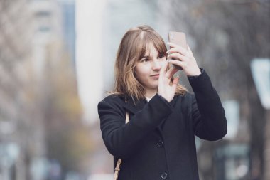 Akıllı telefon kullanan, fotoğraf çeken ve uygulamalar kullanan genç bir kadın.