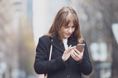 Şehrin sokaklarında akıllı telefon kullanan genç bir kadın.