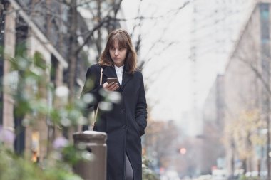Şehrin sokaklarında akıllı telefon kullanan genç bir kadın.