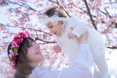 Genç bir beyaz anne ve bebek çiçek açmış bir sıra kiraz çiçeklerinin tadını çıkarıyorlar.