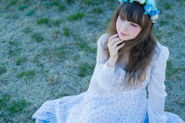 Yeşil topraklarda mavi Corolla giyen beyaz bir kadının portresi.