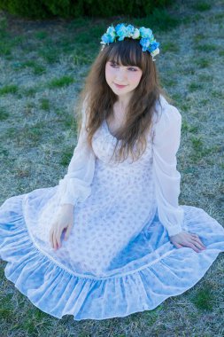 Yeşil topraklarda mavi Corolla giyen beyaz bir kadının portresi.