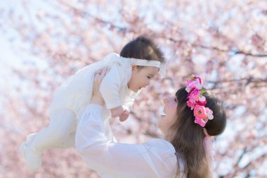 Genç bir beyaz anne ve bebek çiçek açmış bir sıra kiraz çiçeklerinin tadını çıkarıyorlar.