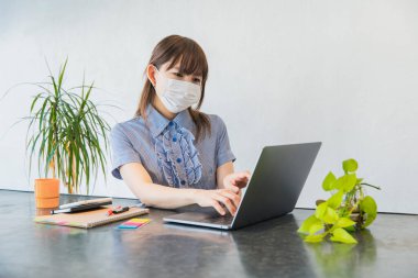 Maske takan ve evdeki oturma odasında uzaktan çalışan bir kadın.