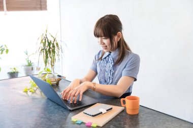 Asyalı kadın evdeki oturma odasında masa başı işi yapıyor.