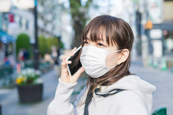スマートフォンの呼び出し機能をマスクで使用するアジアの女性 — ストック写真