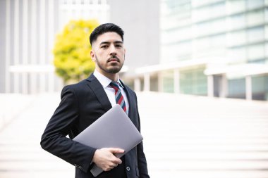 Karışık ırk genç işadamı, takım elbiseli, dizüstü bilgisayar kullanıyor.