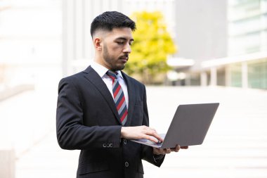 Karışık ırk genç işadamı, takım elbiseli, dizüstü bilgisayar kullanıyor.