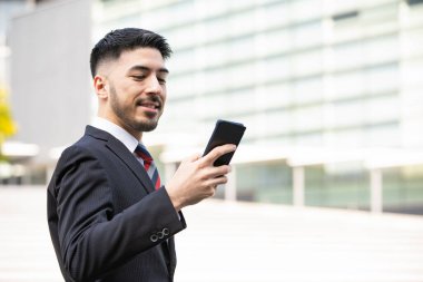 Akıllı telefon kullanan, takım elbiseli, melez, genç bir işadamı.