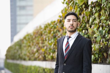 Açık havada duran, sakallı, melez, genç bir iş adamı.